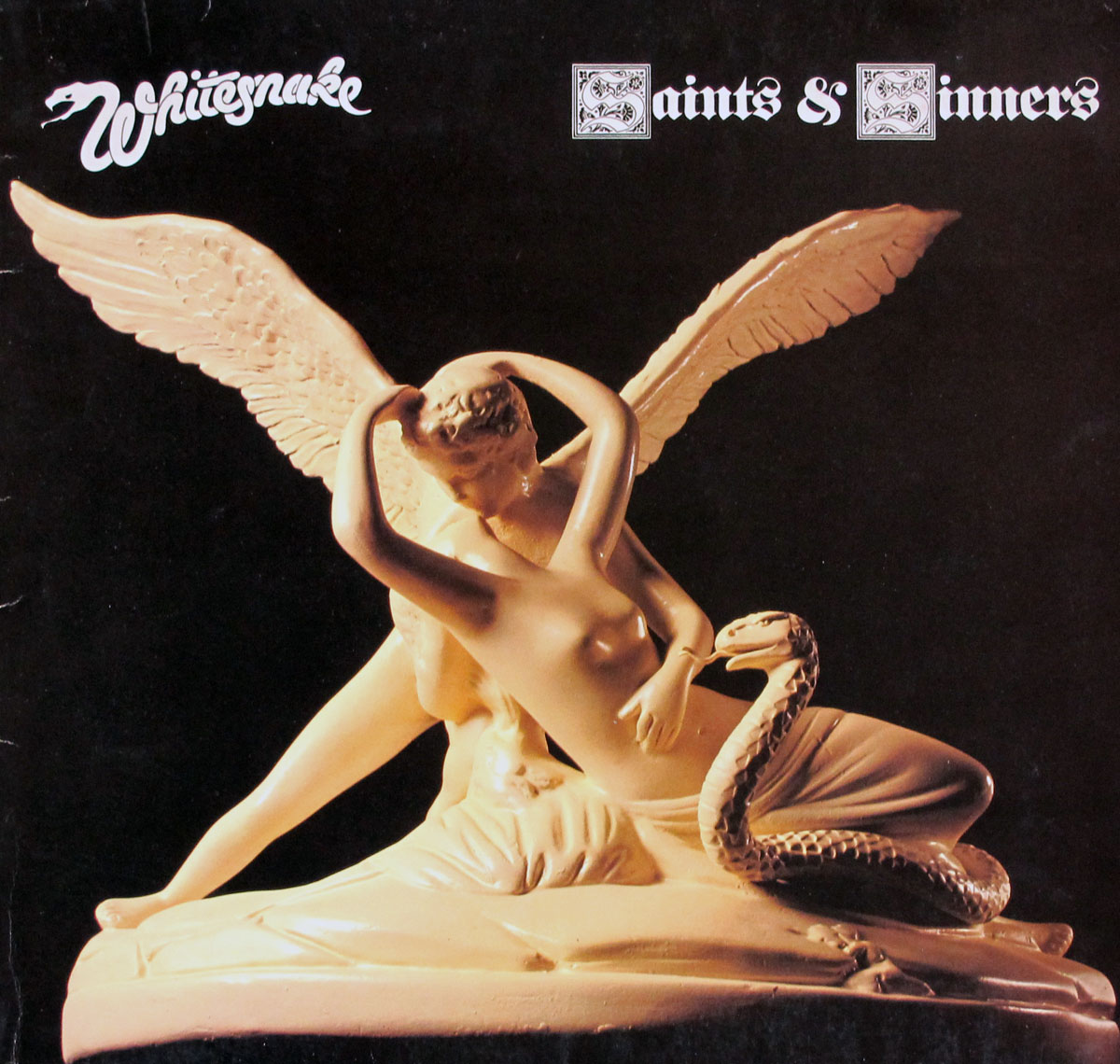Album cover for Whitesnake's Saints & Sinners, featuring a classical-style sculpture of a winged angel embracing a nude female figure who is entwined with a snake. The cream-colored statue stands out against a dark background, with the Whitesnake logo in the top left corner and the album title in gothic font on the right.